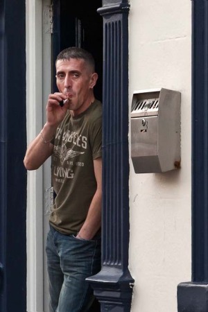Man in doorway of Pub with pram and smoking cigarette